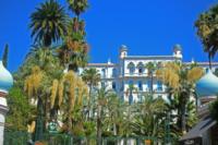 Cannes white building hotel stands among palm trees.
